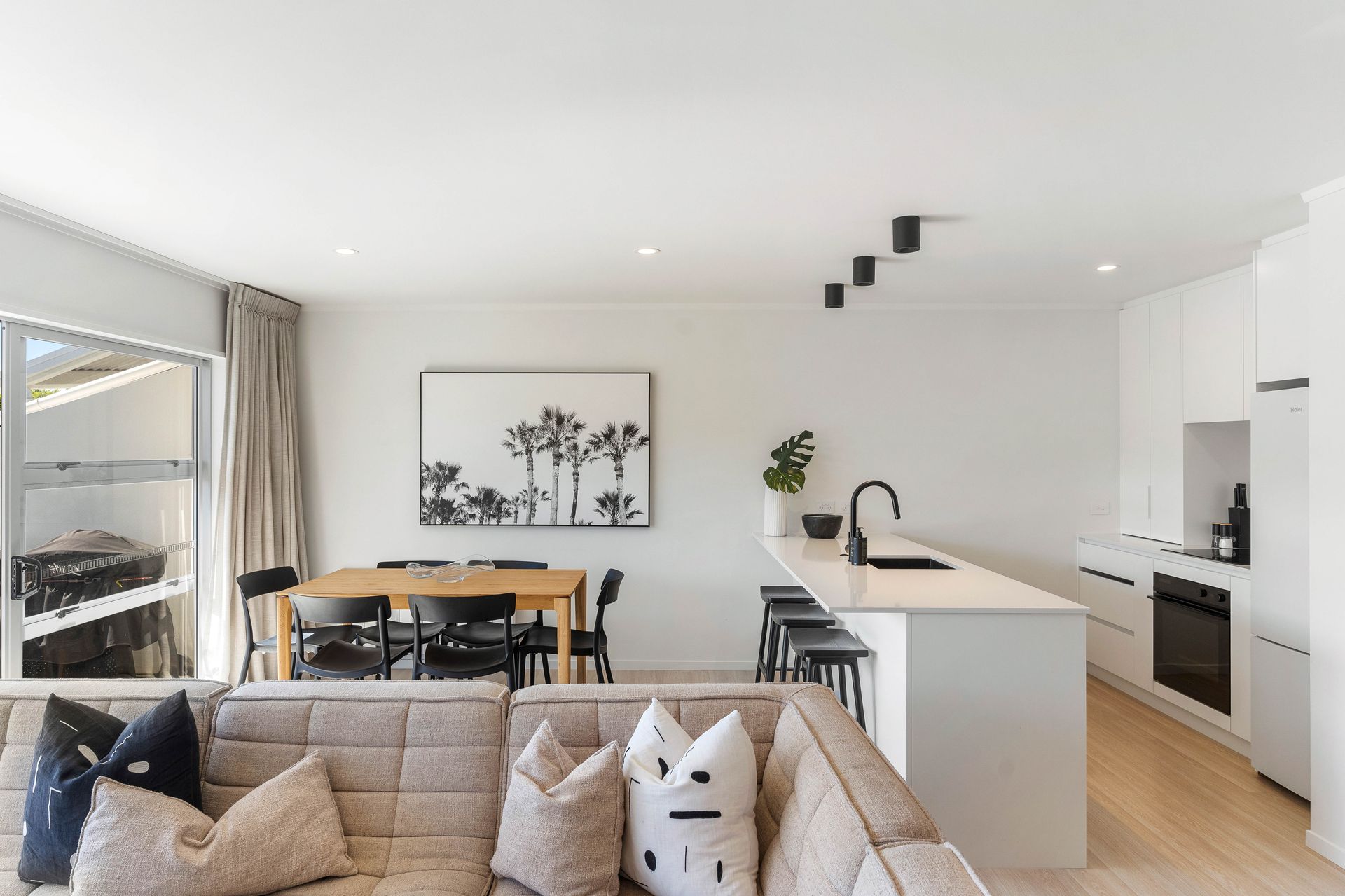 Modern open-plan living space with a kitchen, dining area, and living room. Neutral tones and natural light.