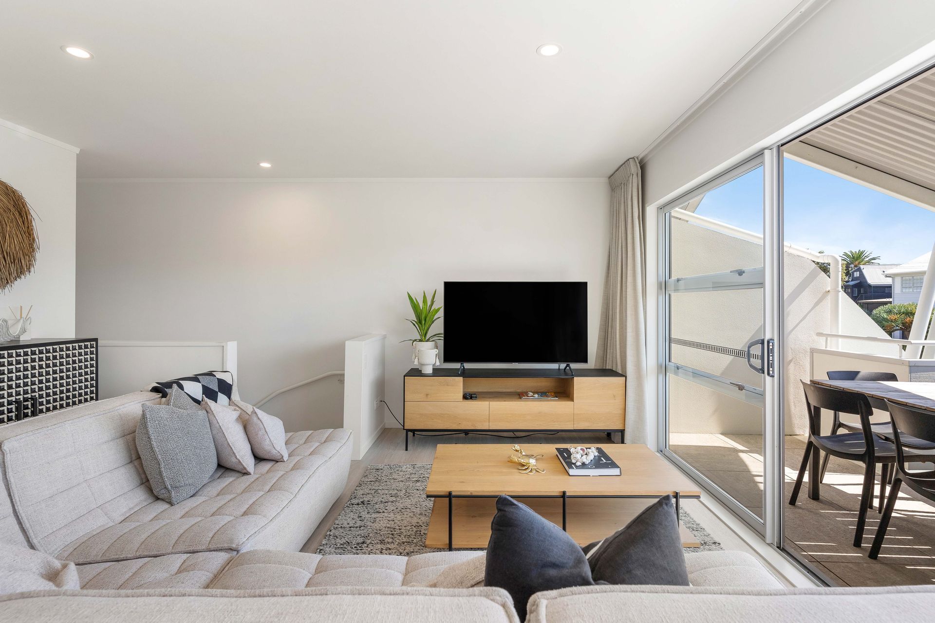 Living room with beige sofa, TV, and sliding door to a balcony with table and chairs.