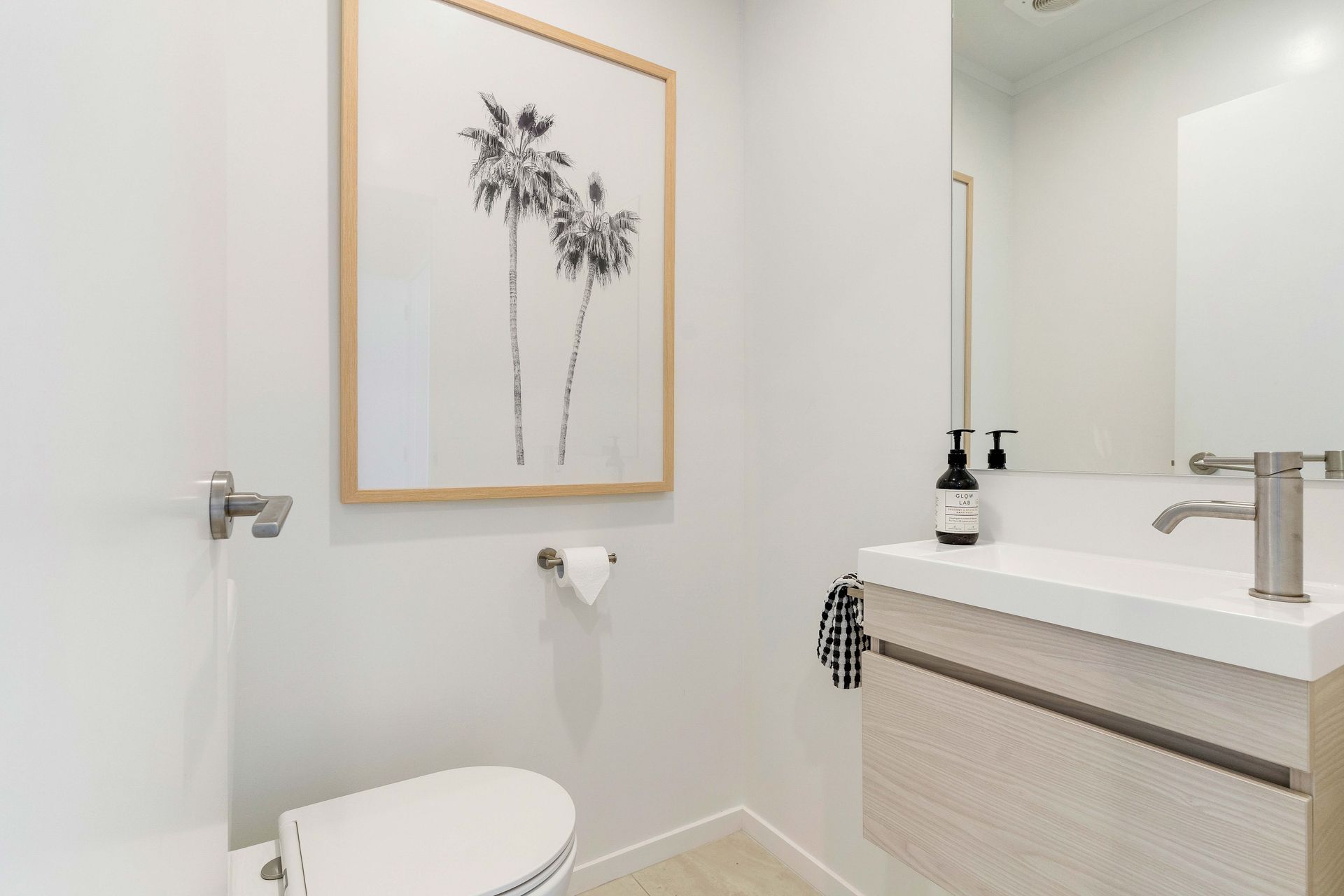 Small, modern bathroom with white walls, a framed palm tree print, and a floating sink.
