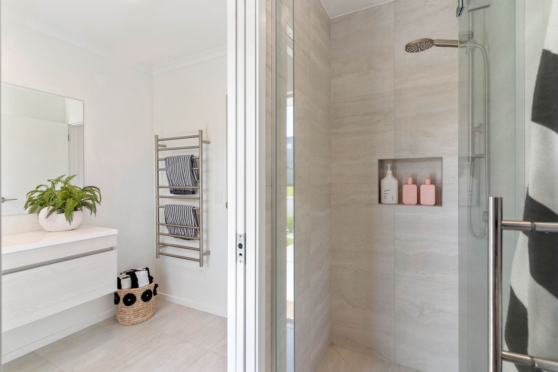 Modern bathroom with a glass shower, neutral tile, and heated towel rack.