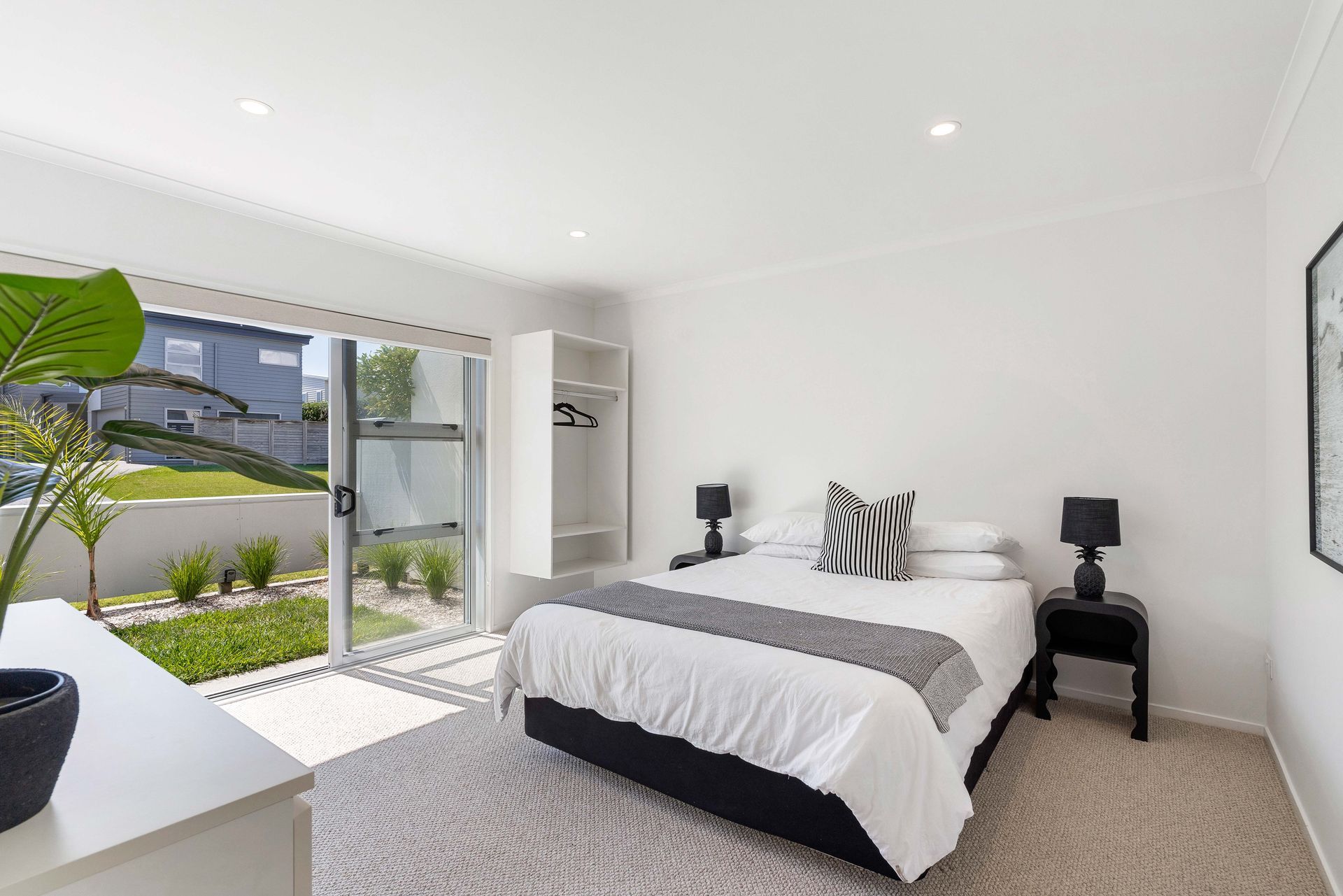 Bright, modern bedroom with a bed, small closet, and sliding glass doors leading to a yard.