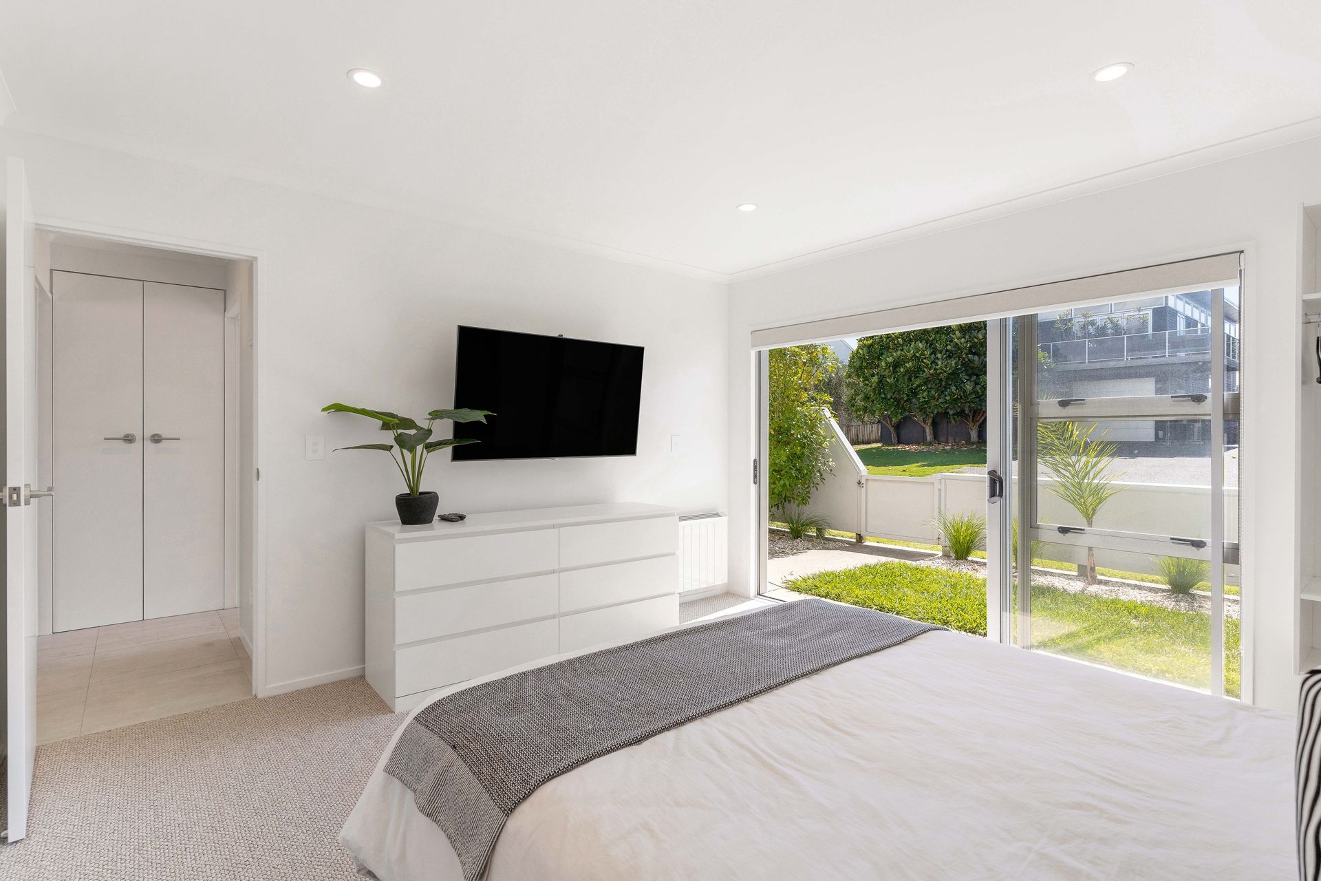 Bedroom with white walls, a bed with gray blanket, dresser, and sliding glass doors to a backyard.
