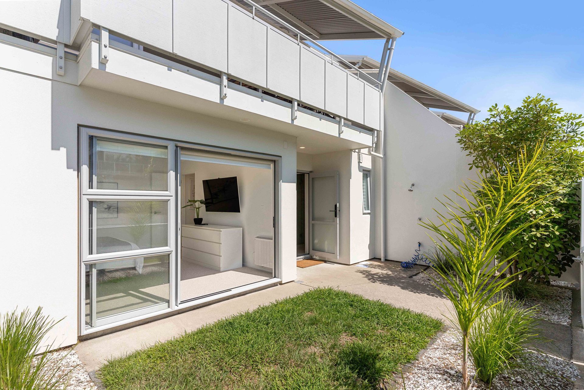 Exterior of a modern, white building with open sliding glass doors leading to a room with a TV.