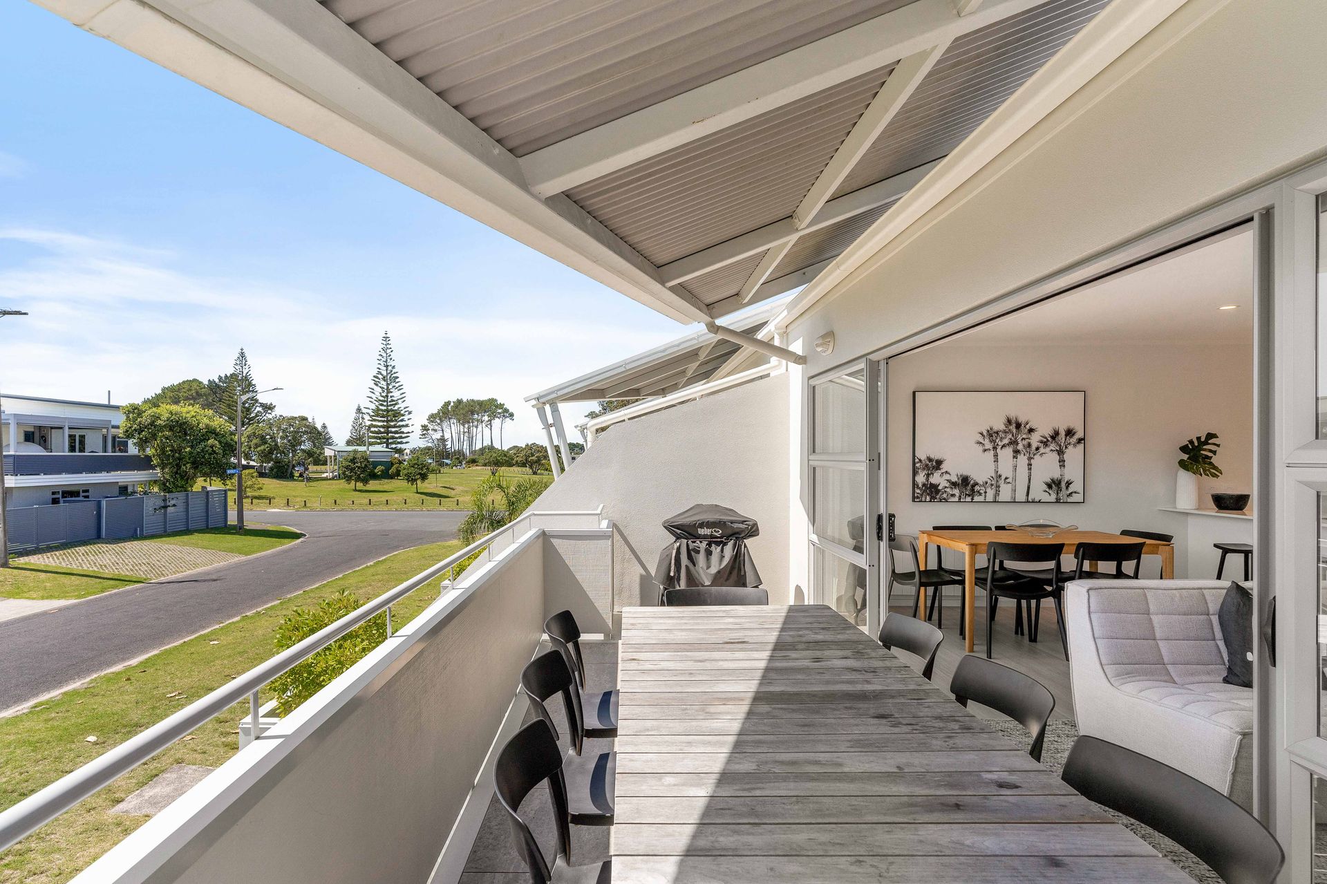 Balcony overlooking a road and greenery, connected to a dining room.