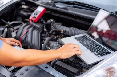 Un uomo sta lavorando al motore di un'auto con un laptop.