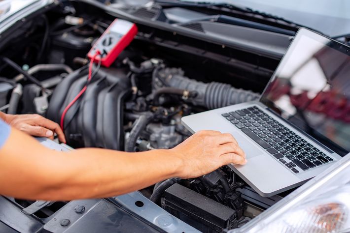 Un uomo sta lavorando al motore di un'auto con un laptop.