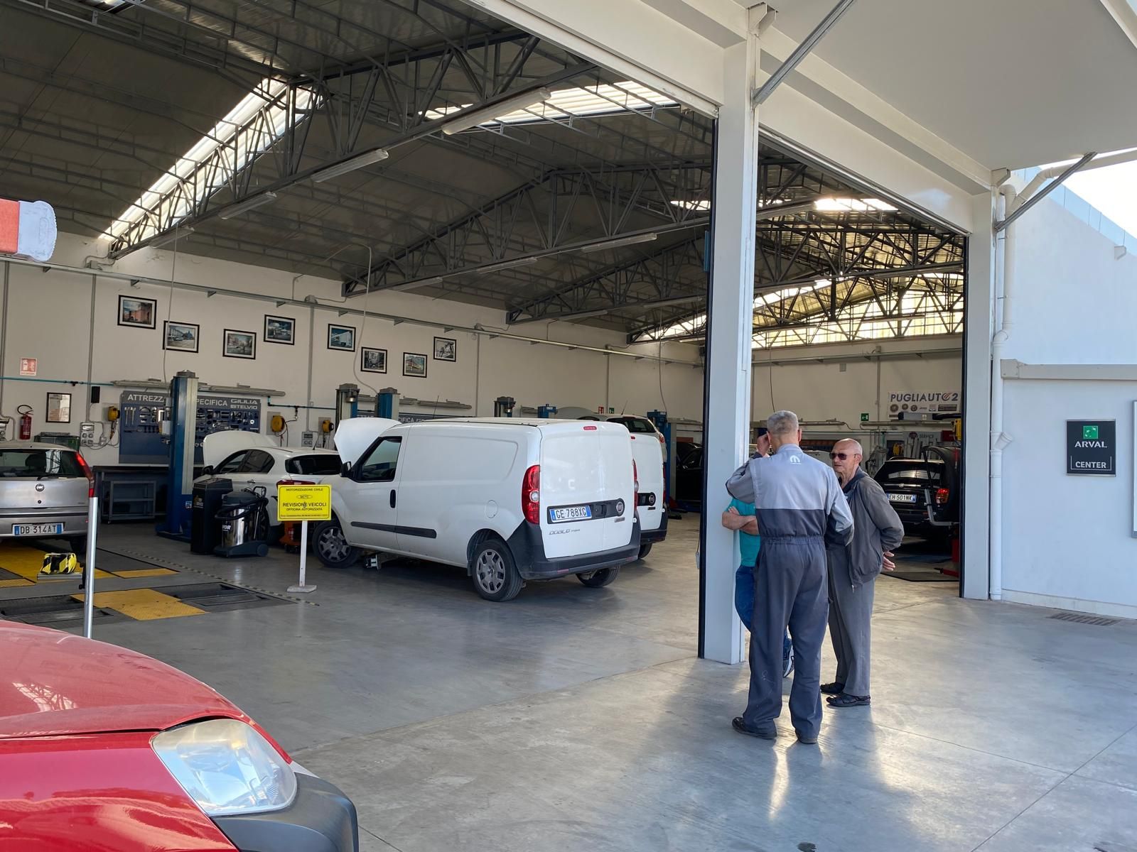 Un gruppo di persone è in piedi in un garage accanto a un'auto rossa.
