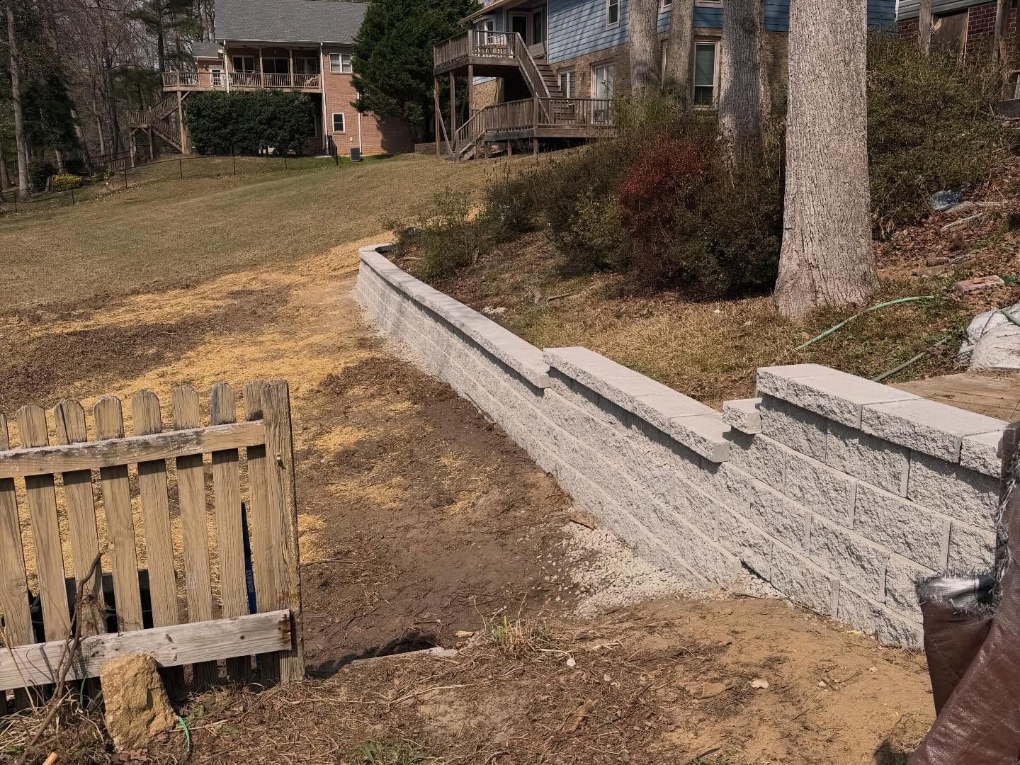 Stone retaining wall along a grassy yard beside a basement stairwell and house