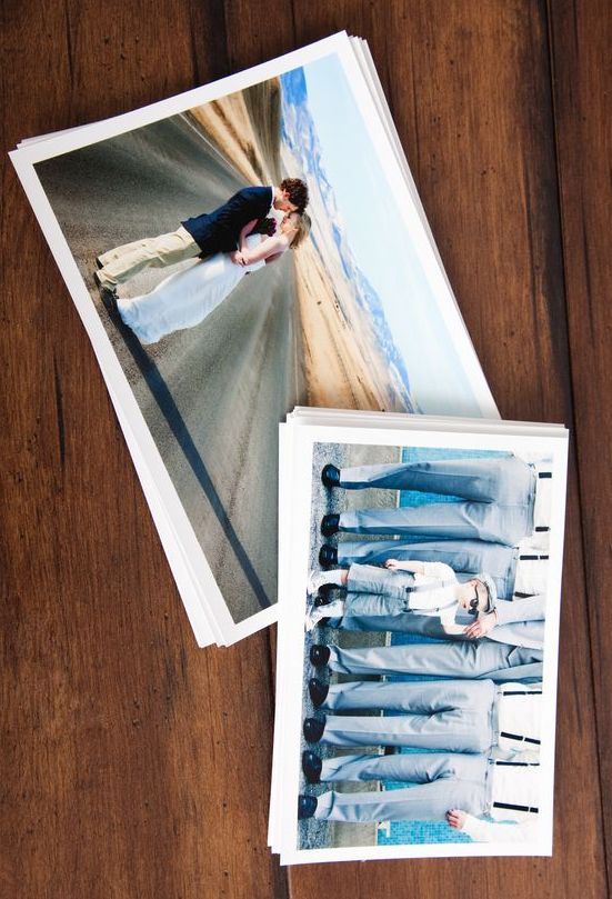 Stacks of wedding photos on wood: couple kissing on road, groomsmen in suits.
