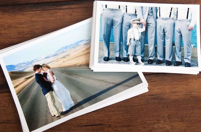 Stack of printed wedding photos on a wood table, featuring couple embracing on road and groomsmen with a child.
