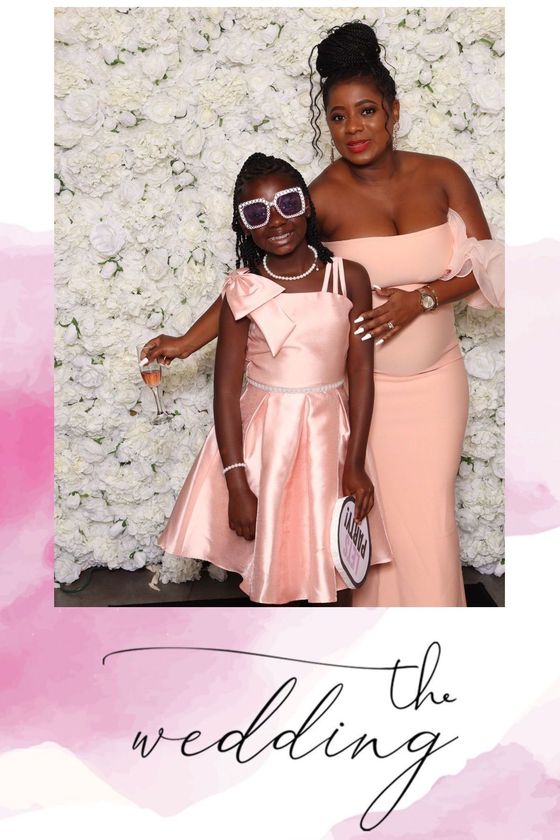 Woman and girl in pink dresses posing in front of a flower wall at a wedding.