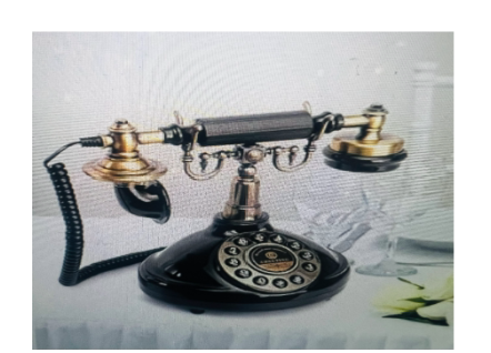 Antique black and brass rotary phone on a white table.