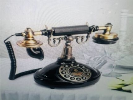 Antique black and brass rotary phone on a white table.