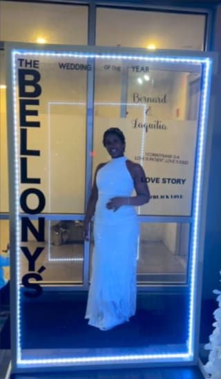 Woman in a white dress smiling, standing inside a lit frame advertising a wedding.
