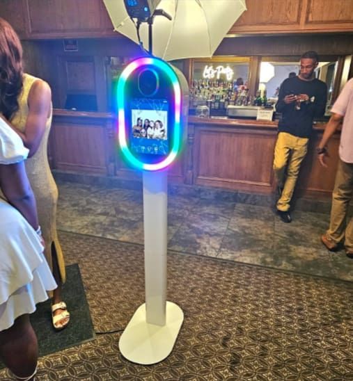 Photo booth at a party with people. A rainbow light circle surrounds the screen.