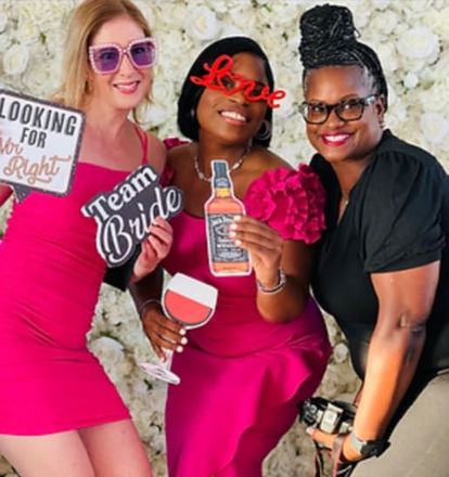 Three women in front of a flower wall holding photo props.
