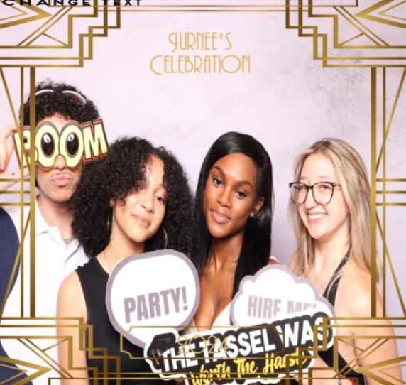 Four people posing in a photo booth. Two hold speech bubbles. Deco-style frame.