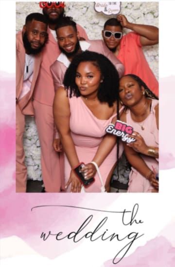 Group photo at a wedding with people in blush tones and a floral backdrop.