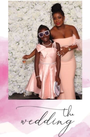 Woman and girl in pink dresses posing in front of a flower wall at a wedding.