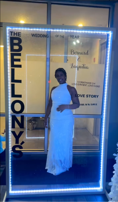 Woman in a white dress smiling, standing inside a lit frame advertising a wedding.