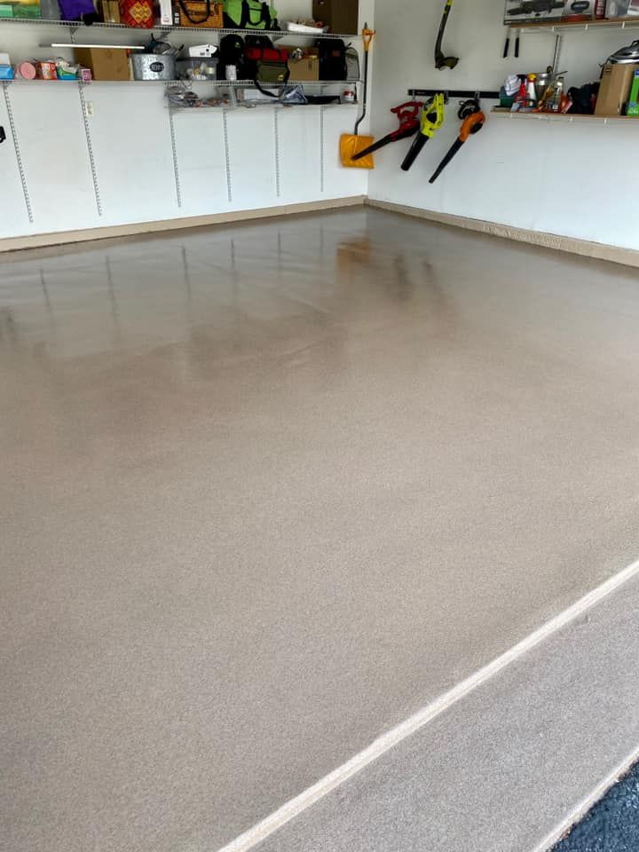 A clean, beige-colored epoxy garage floor with overhead storage shelves and wall-mounted tools in the background.