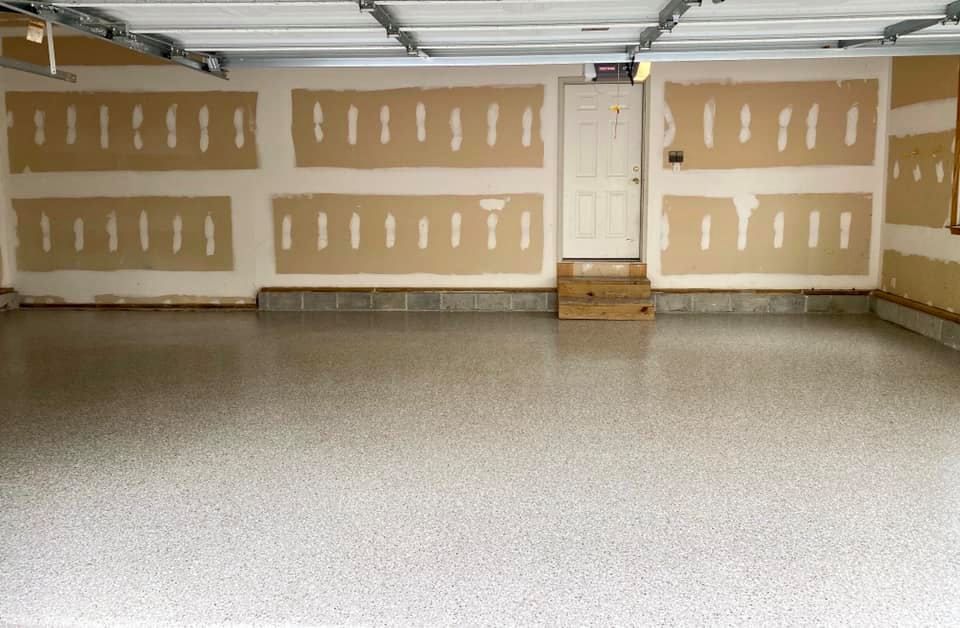 A spacious, clean garage featuring a gray speckled epoxy floor and unfinished drywall with taped joints.