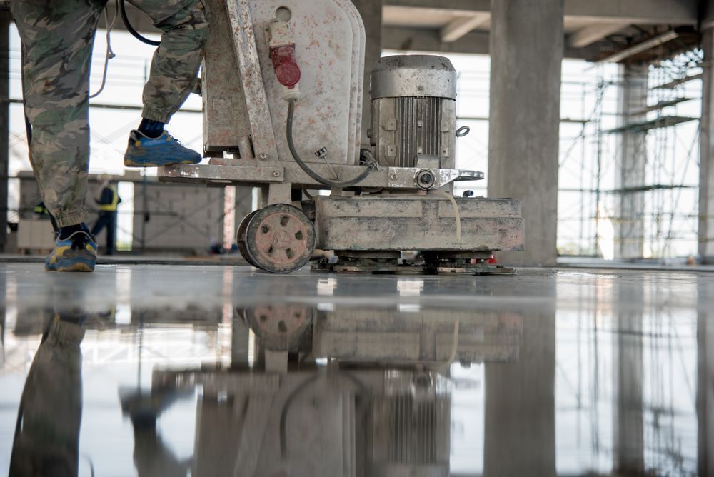 A person operates a floor polishing machine on a highly reflective, polished concrete floor at a construction site.