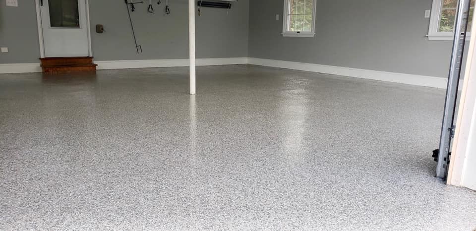 A spacious garage interior featuring a glossy, light grey speckled epoxy floor with grey walls and a white support pole.