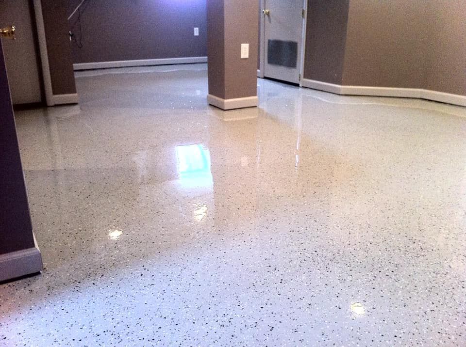 A glossy, white floor with grey and black speckles in a finished basement room with support columns and light-colored walls.
