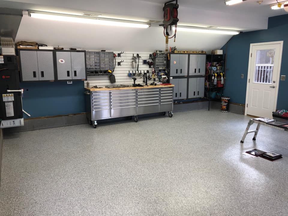 A well-organized garage with grey floors, metallic storage cabinets, a workbench, tools, and a white door on the right.
