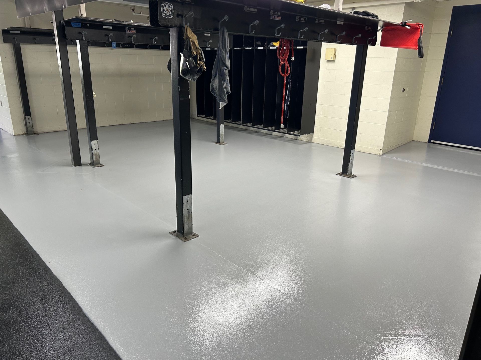 A spacious locker room with a smooth, glossy light gray floor, black support pillars, and rows of open lockers.