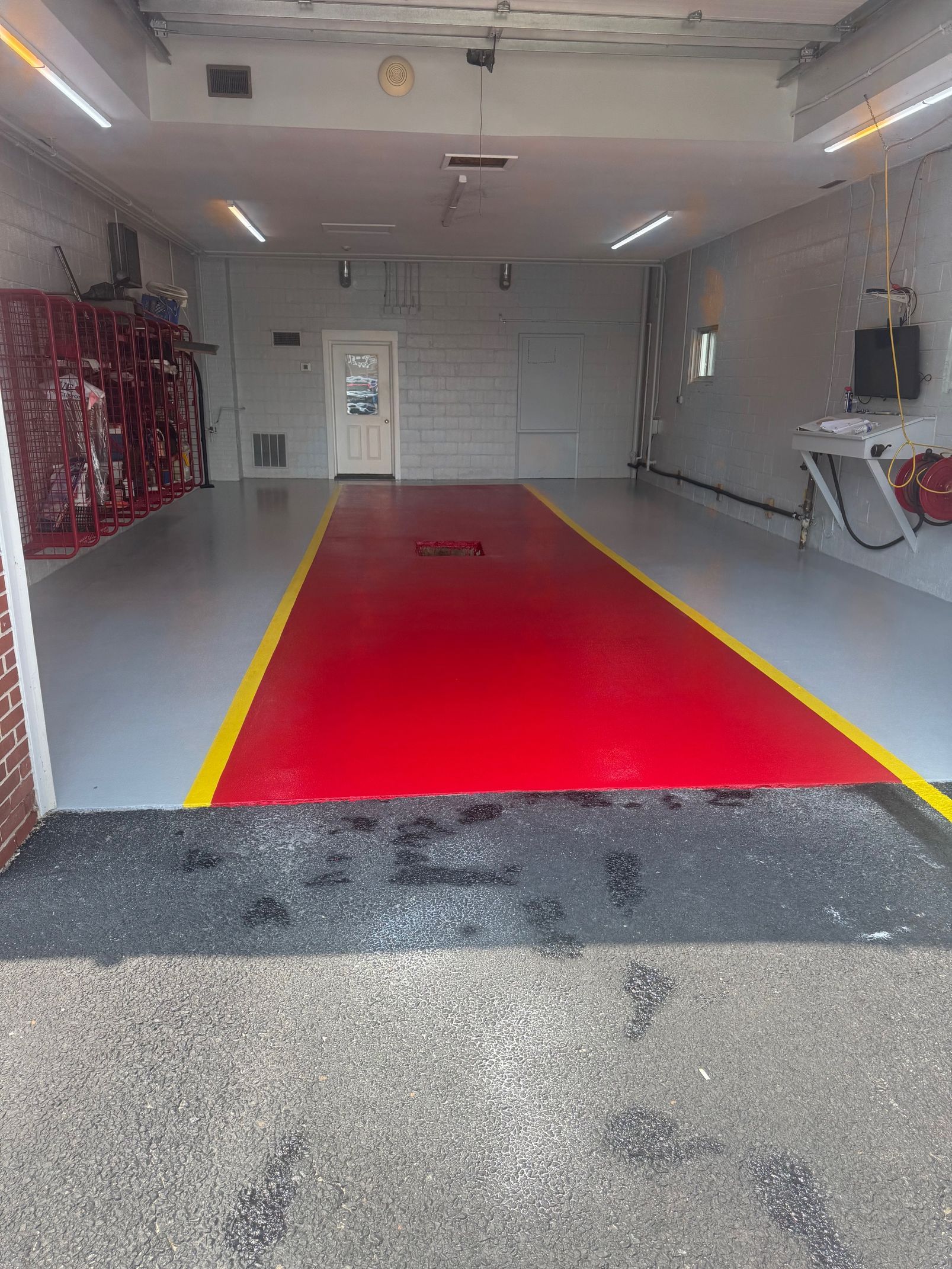A bright, empty garage with a red floor marked by yellow lines, surrounded by grey floor space and white walls.