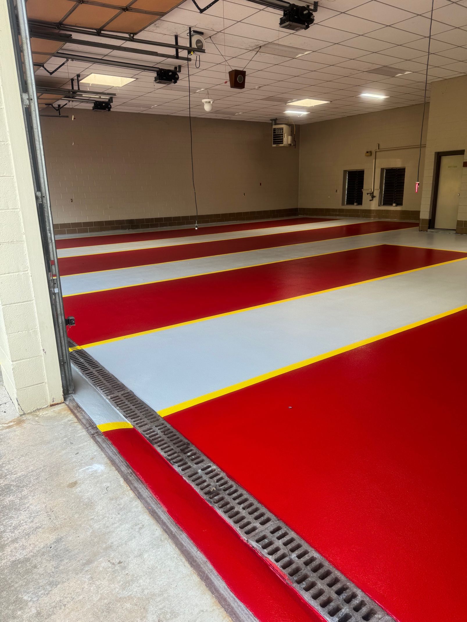 A wide garage interior features a glossy floor with alternating red and light grey stripes separated by thin yellow lines.