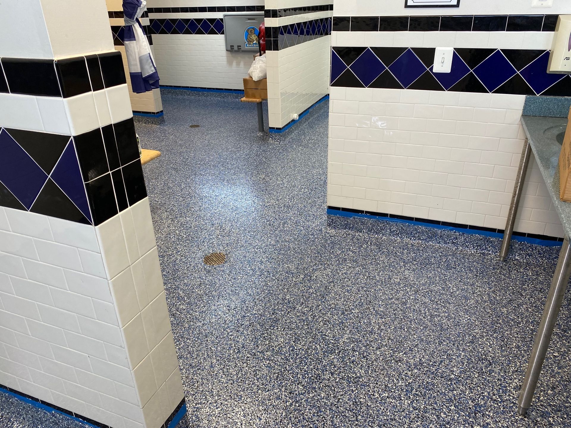 A room with blue-flecked flooring and tiled walls featuring a decorative border of blue and black diamond patterns.