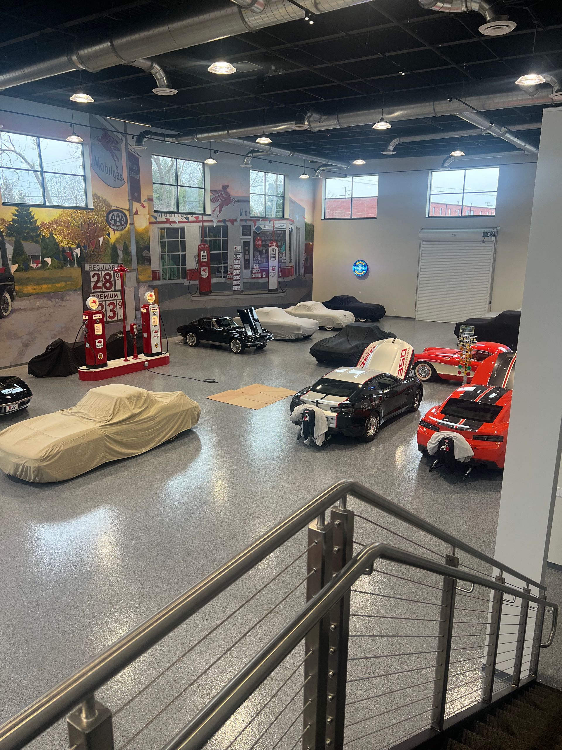 A wide-angle view of a large car storage garage featuring multiple vehicles, some under covers, on a speckled gray floor.