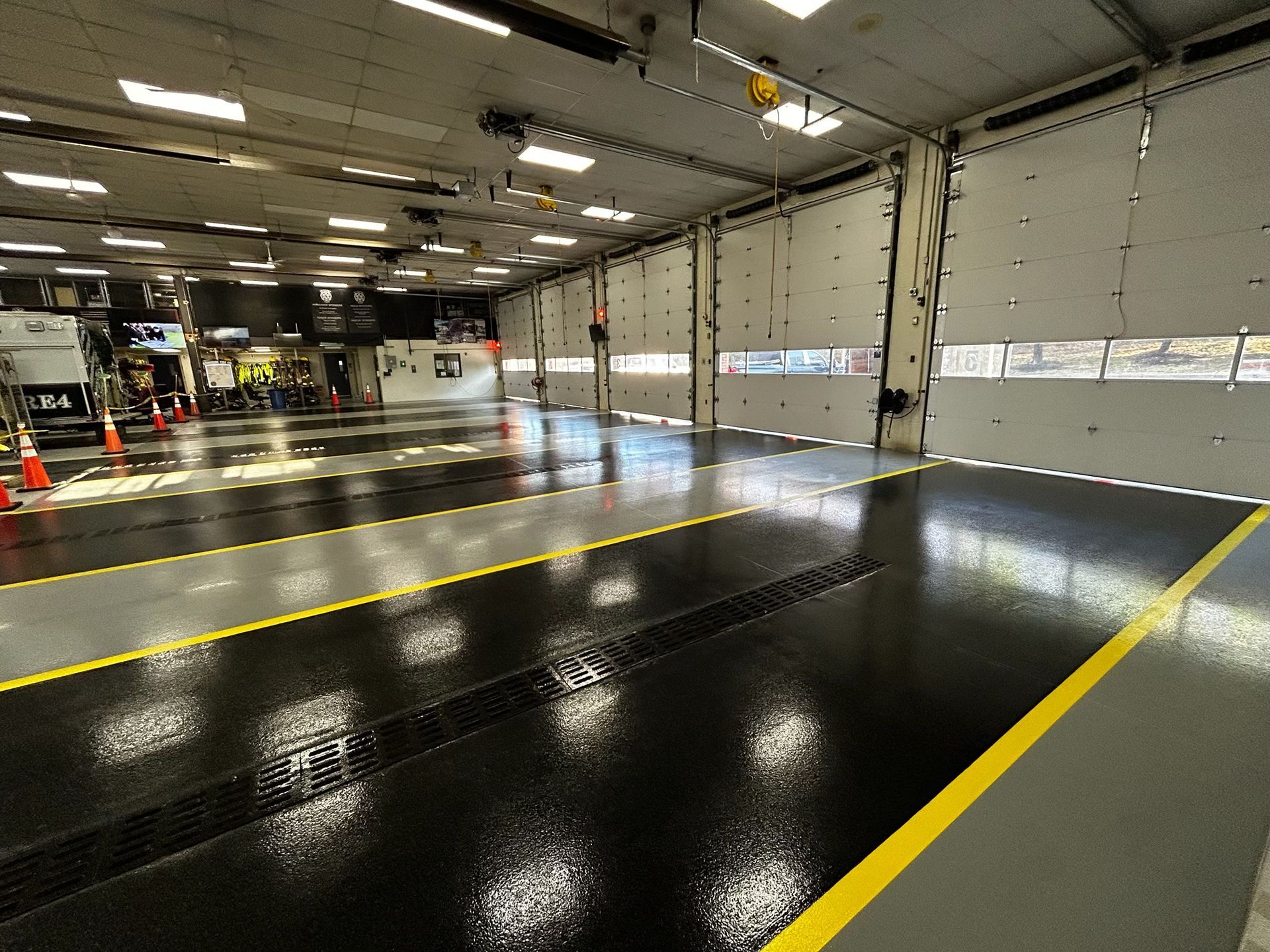 A wide, high-gloss industrial garage bay with black and gray floor segments marked by yellow safety lines.