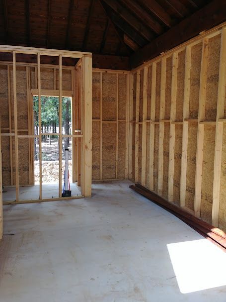 Interior of a room under construction; wood framing, doorframe, and concrete floor.