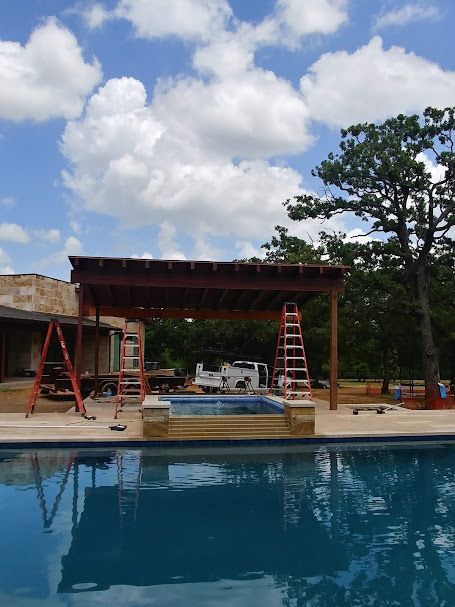 Pergola being constructed over a pool and jacuzzi, under a blue sky with clouds.