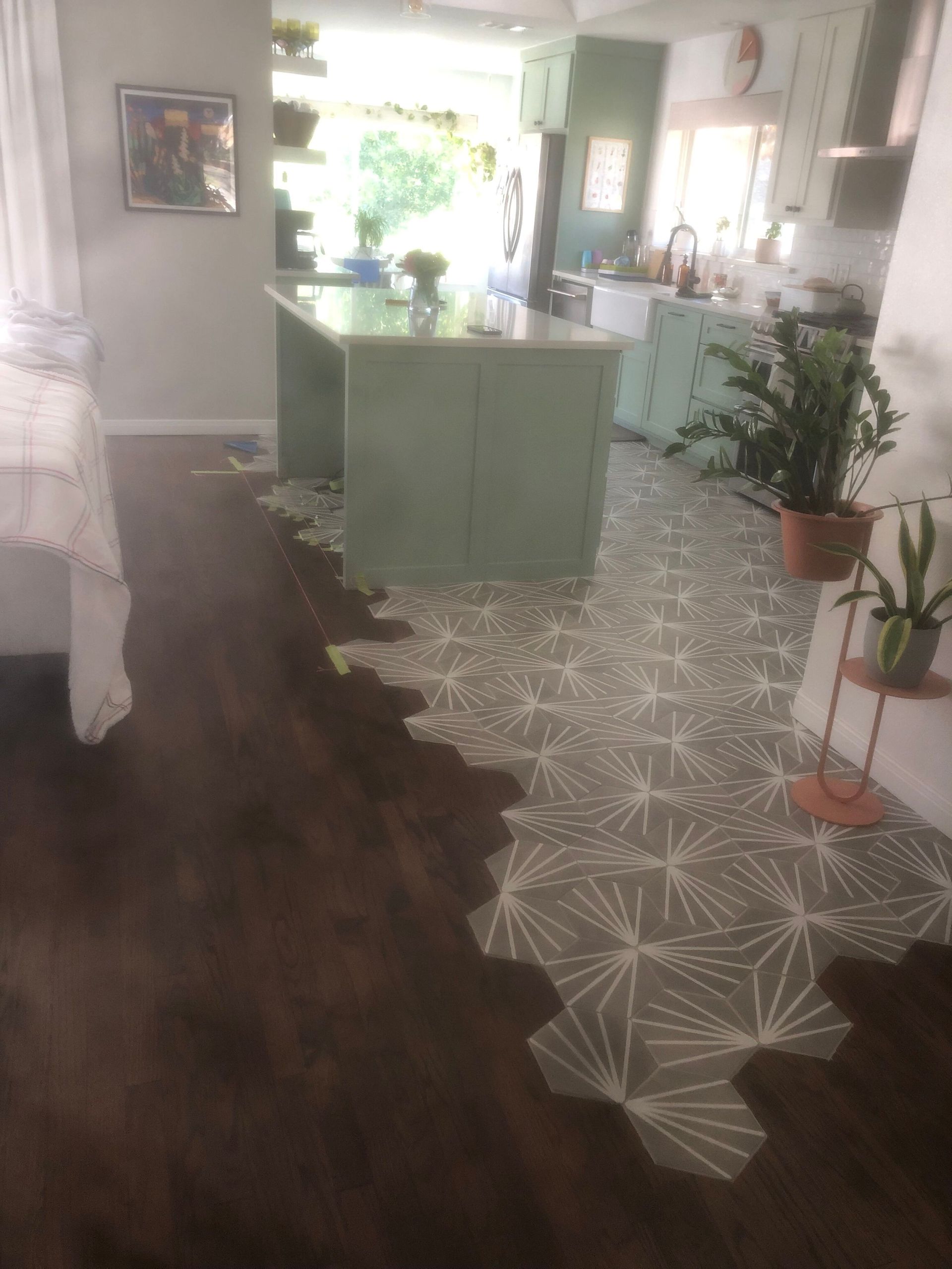 A kitchen with dark wood flooring, a green island, and patterned tile, transitioning between floors.