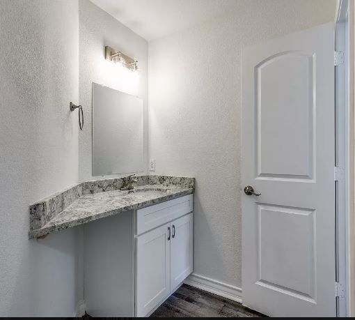 Bathroom with a white vanity, granite countertop, mirror, and a white door.