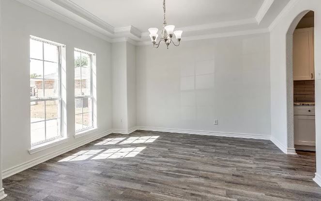 Empty dining room with gray wood-look floors, white walls, windows, and chandelier.
