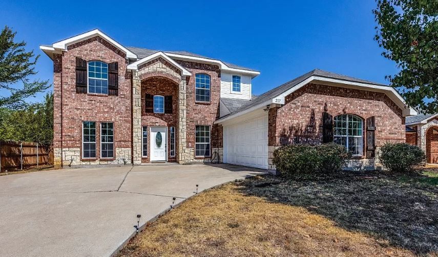 Brick two-story house with a concrete driveway under a bright blue sky.