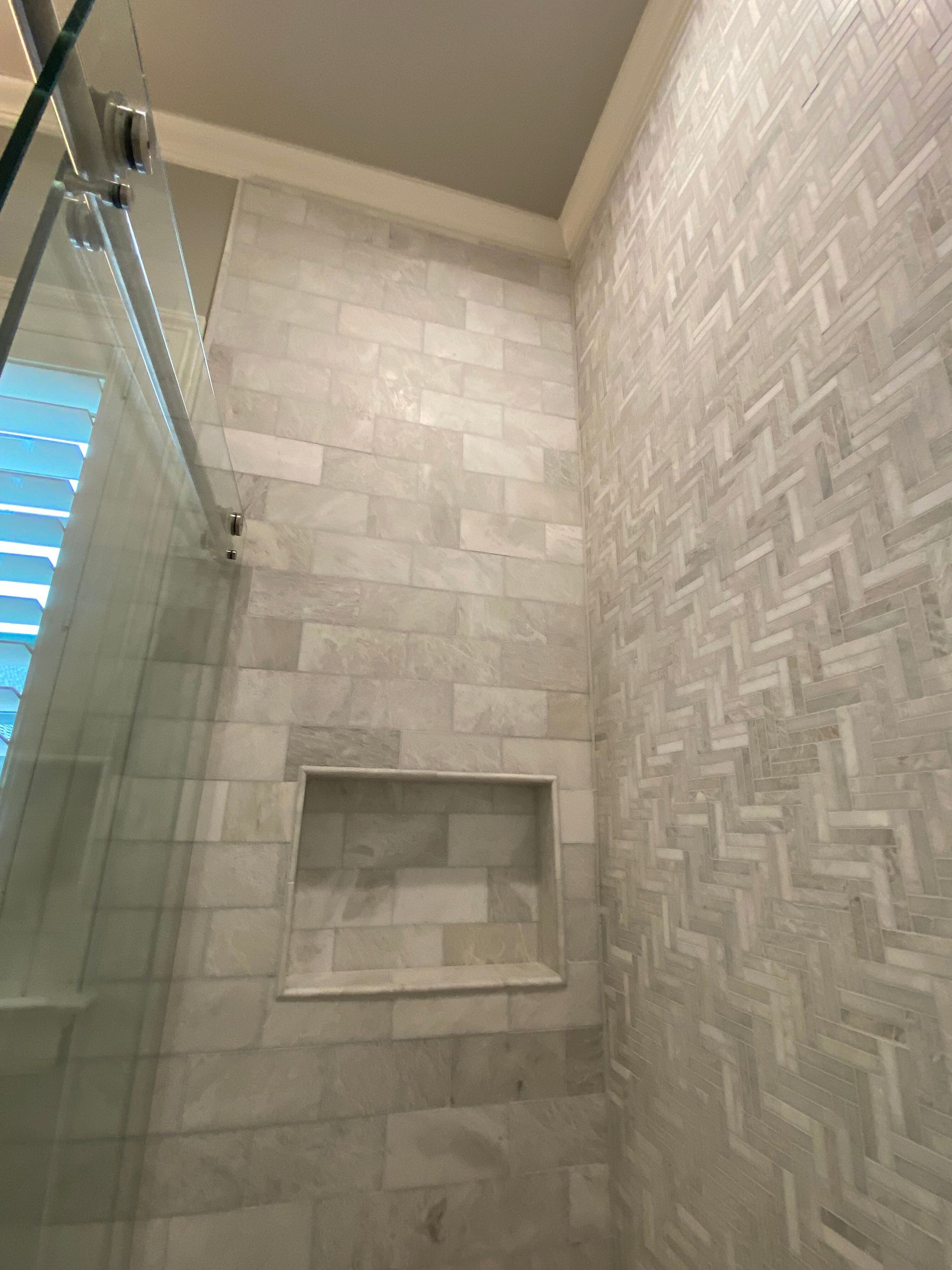 Gray tiled shower with glass door, built-in shelf, and herringbone pattern wall.