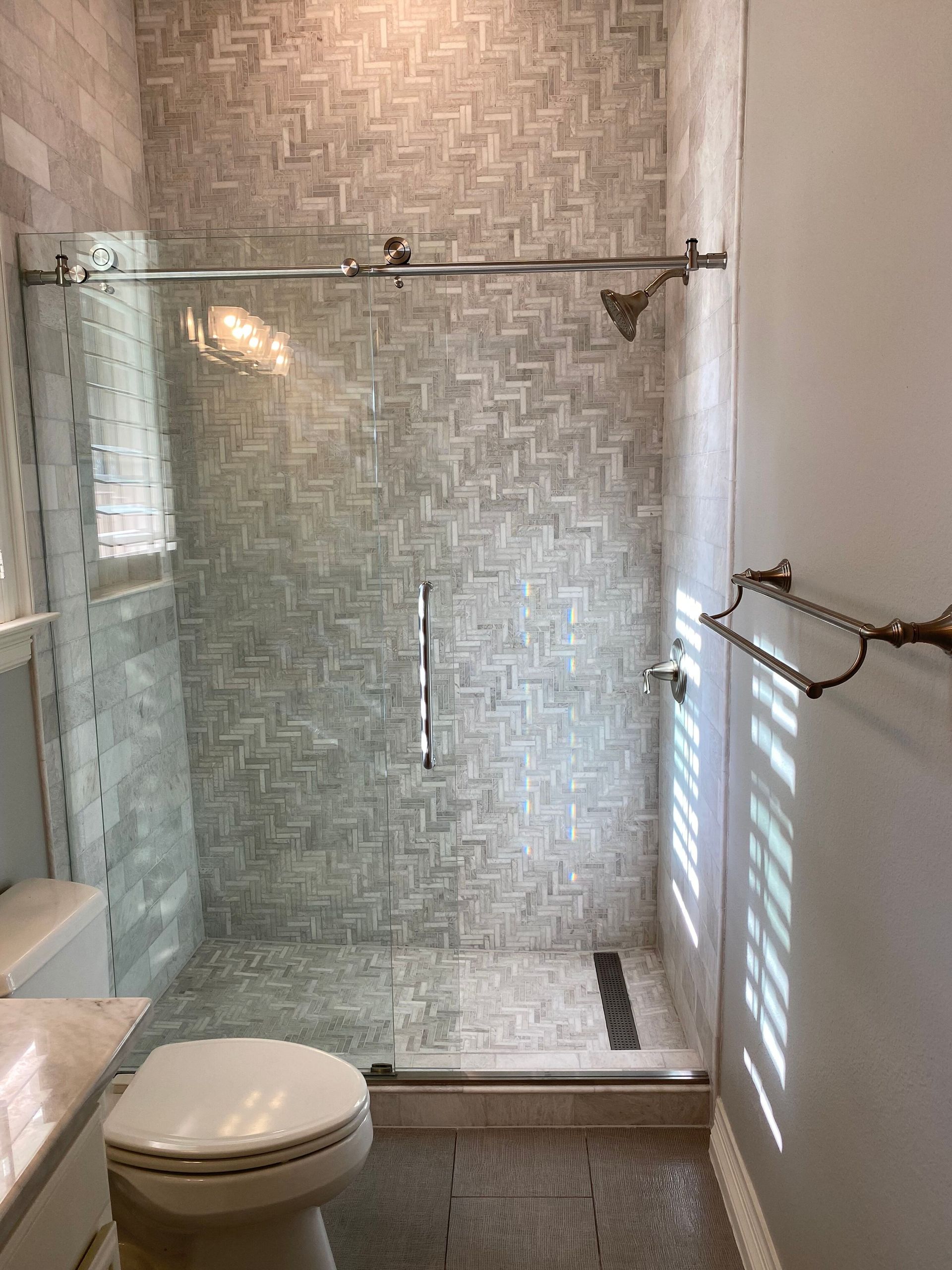 Bathroom with glass shower, patterned tile, and bronze fixtures.
