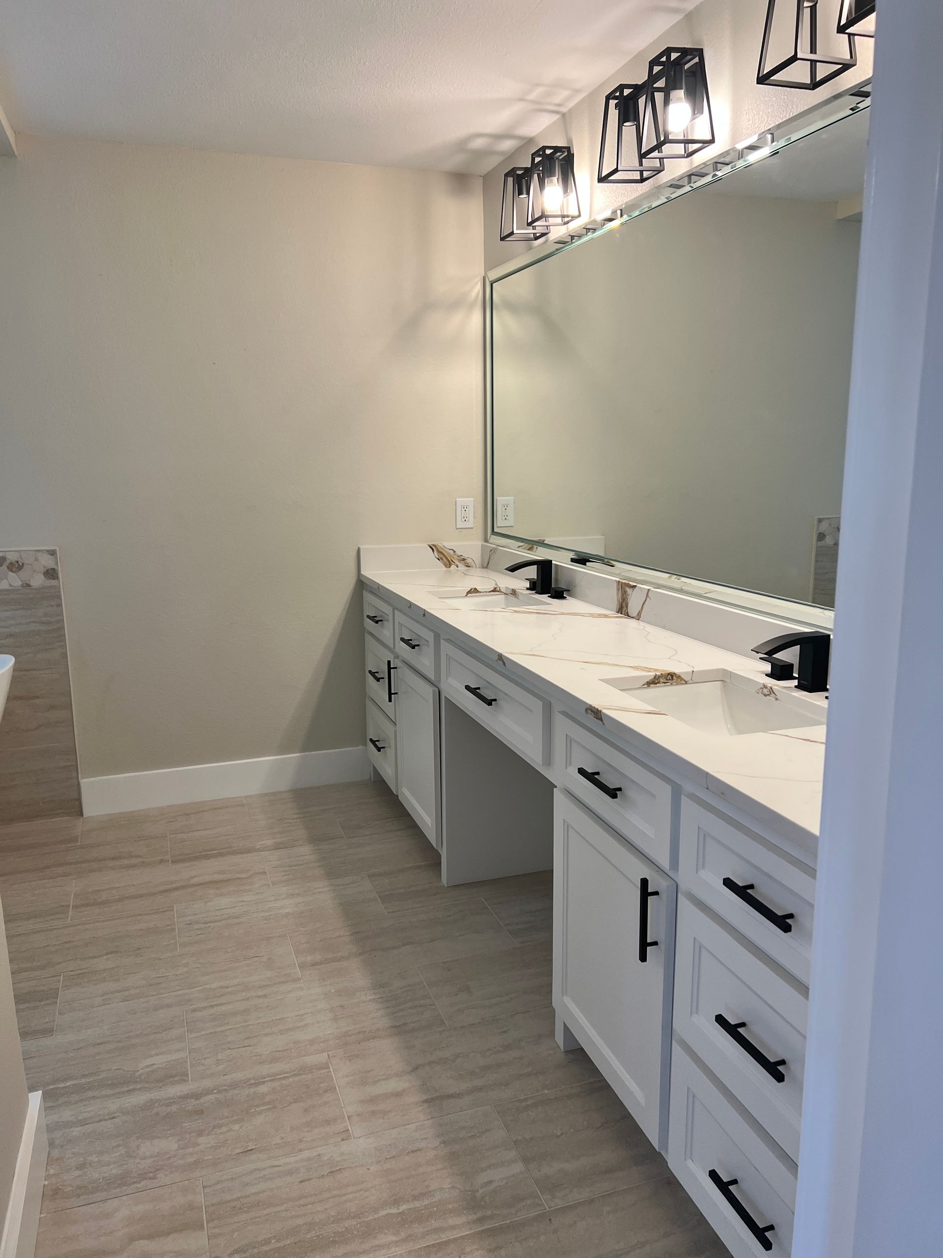 White bathroom vanity with black hardware, large mirror, and overhead lighting.