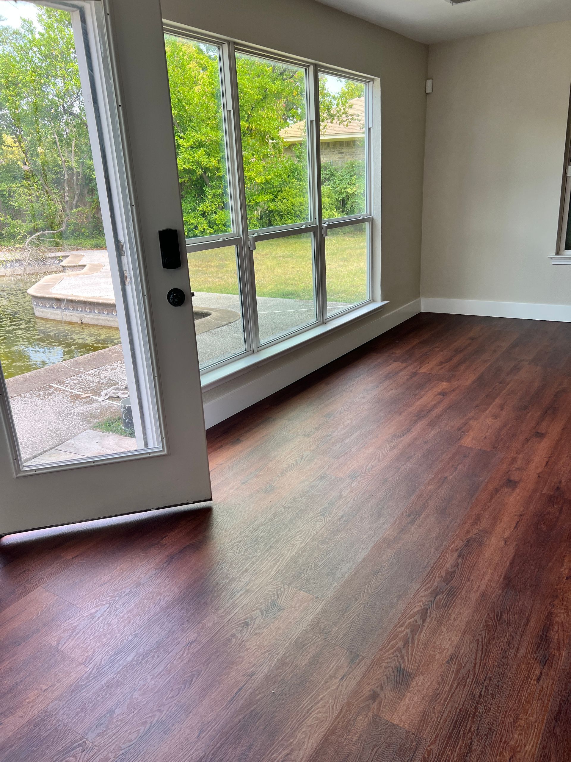 Dark wood floor in a room with large windows and a door to an outdoor area with water and greenery.