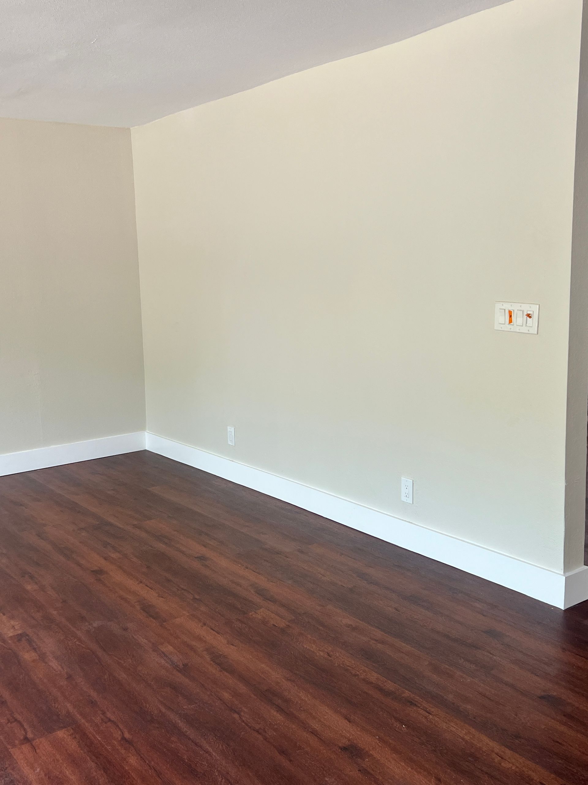 Empty room with dark wood floors, white trim, and beige walls.