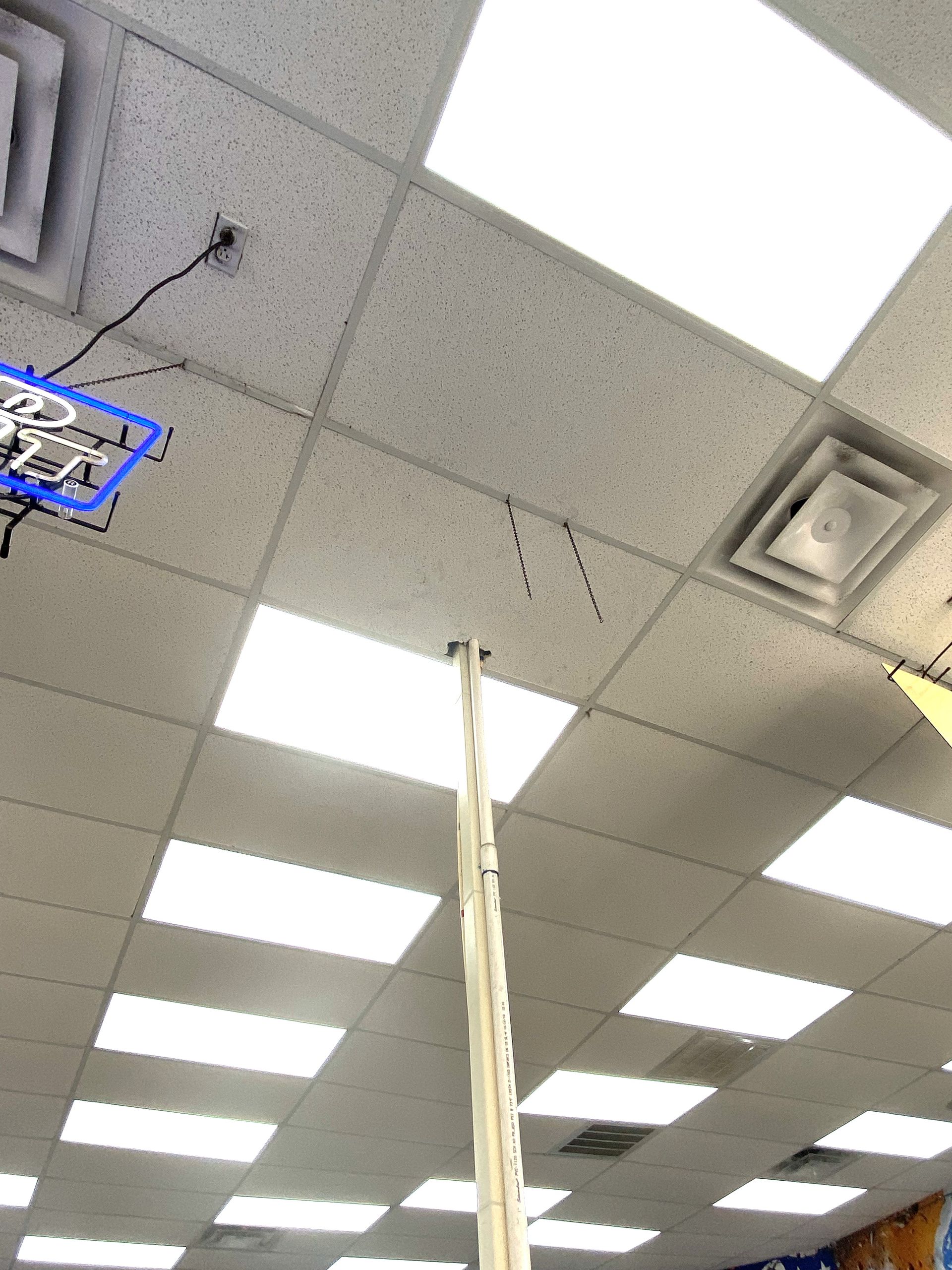 Looking up at a white ceiling with fluorescent lights and a tall, silver pole extending down.