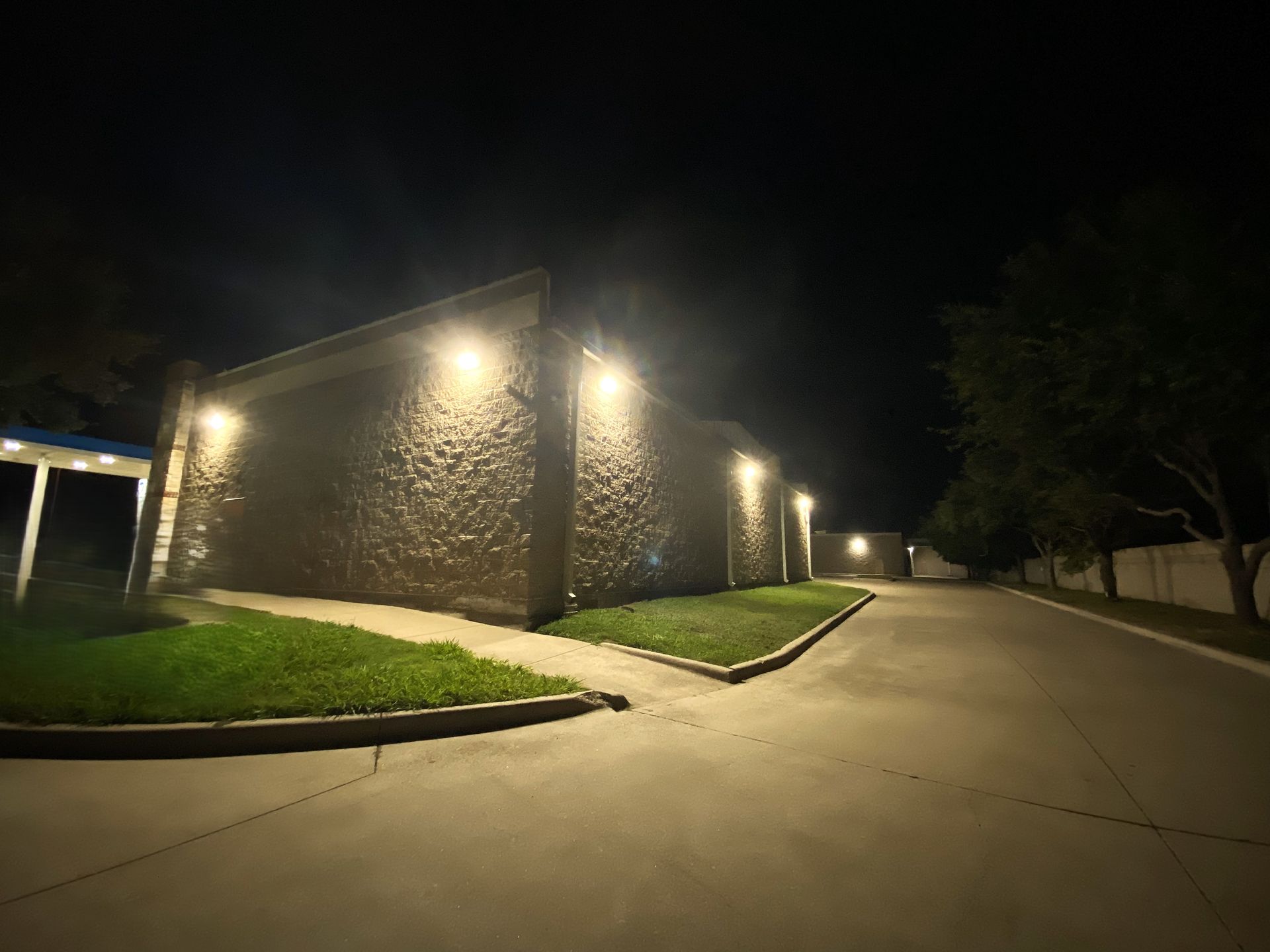 A low-lit building at night with stone walls, lit by spotlights along a curving walkway and grassy area.