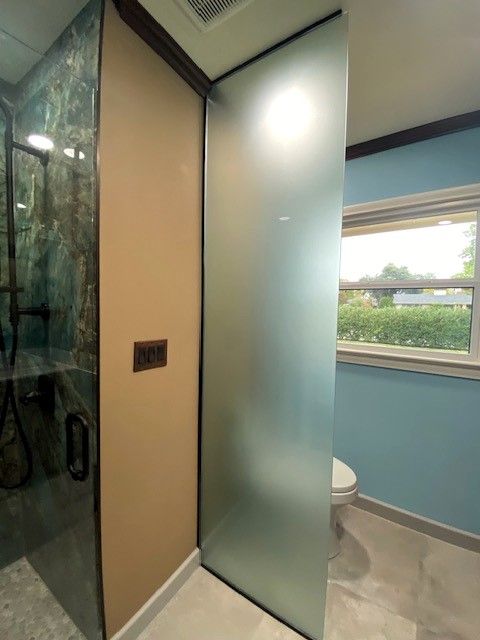 Bathroom with a frosted glass shower divider, toilet, and a window.